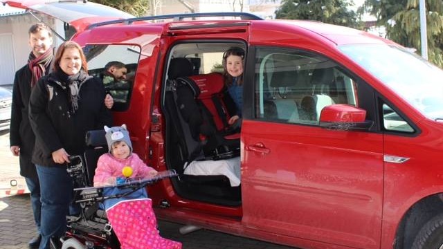 Elisa mit ihrer Familie vor dem ausgebauten Auto mit Rollstuhlrampe und Schiebetür